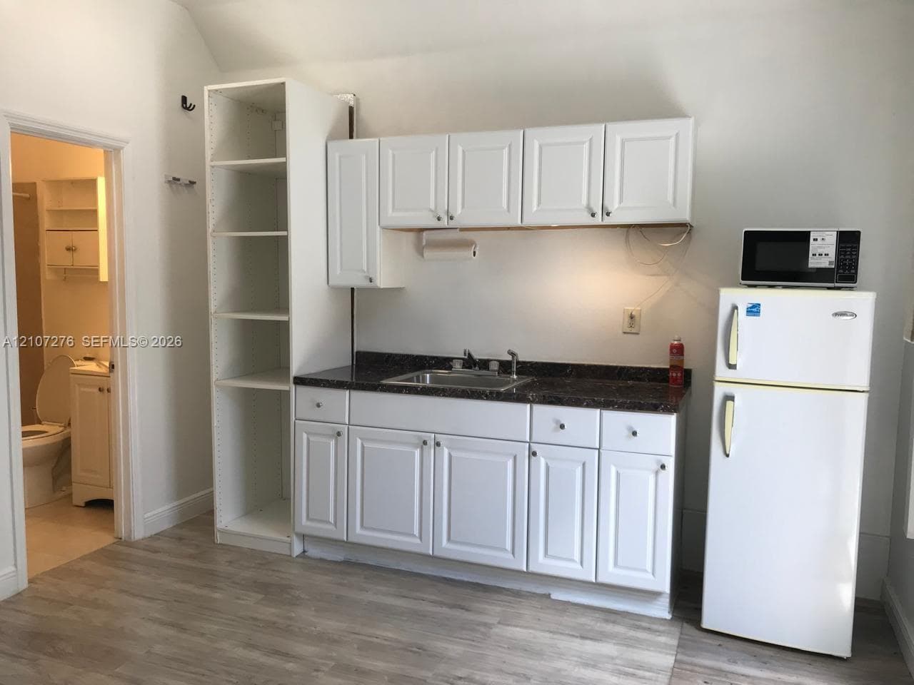 Kitchenette featuring white cabinetry, dark stone-finish countertops, stainless steel sink, built-in shelving, and wood-finish flooring
