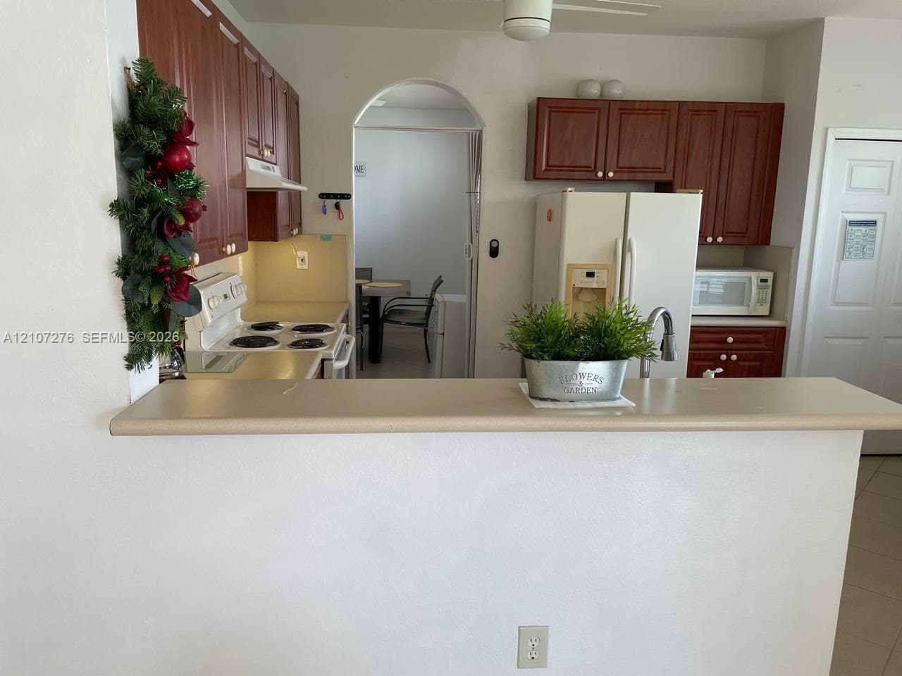 Kitchen featuring cherry-finish cabinetry, solid-surface countertops, breakfast bar, arched entryway, and ceiling fan