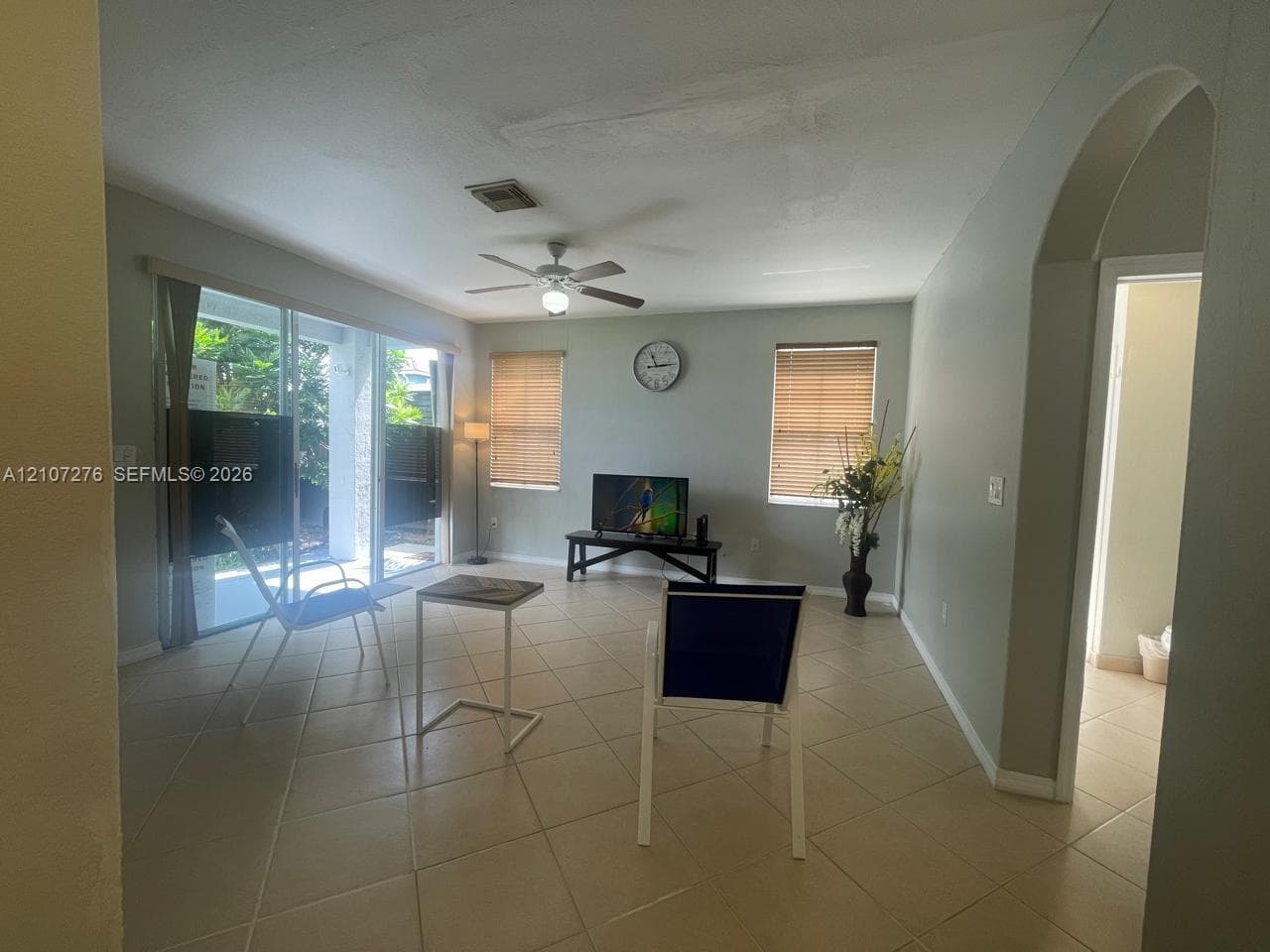 Neutral-toned interior featuring large-format diagonal tile flooring, sliding glass patio doors, a ceiling fan with integrated lighting, and a decorative arched entryway