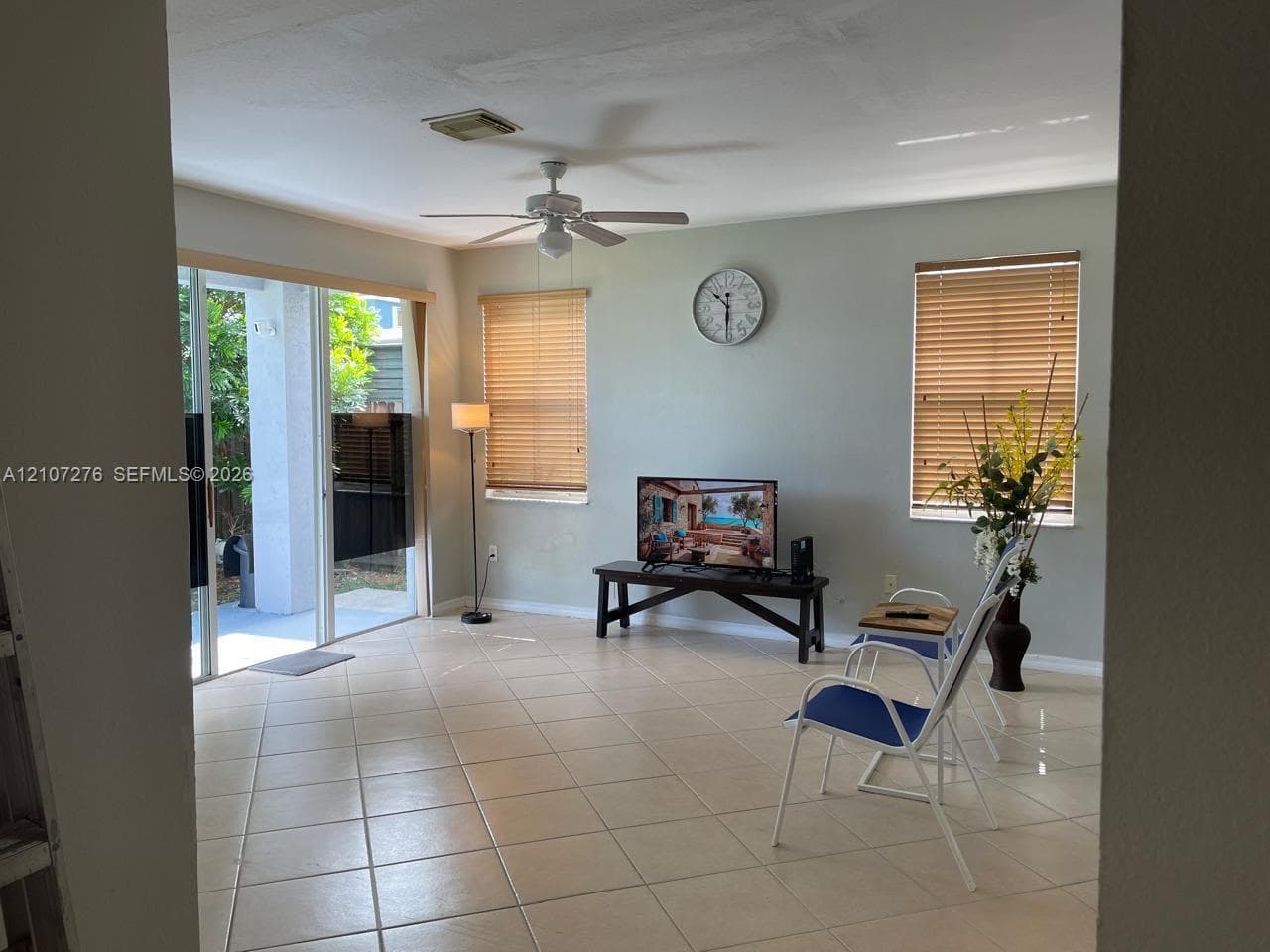 Living area featuring tile flooring, sliding glass doors, dual windows with blinds, and a ceiling fan