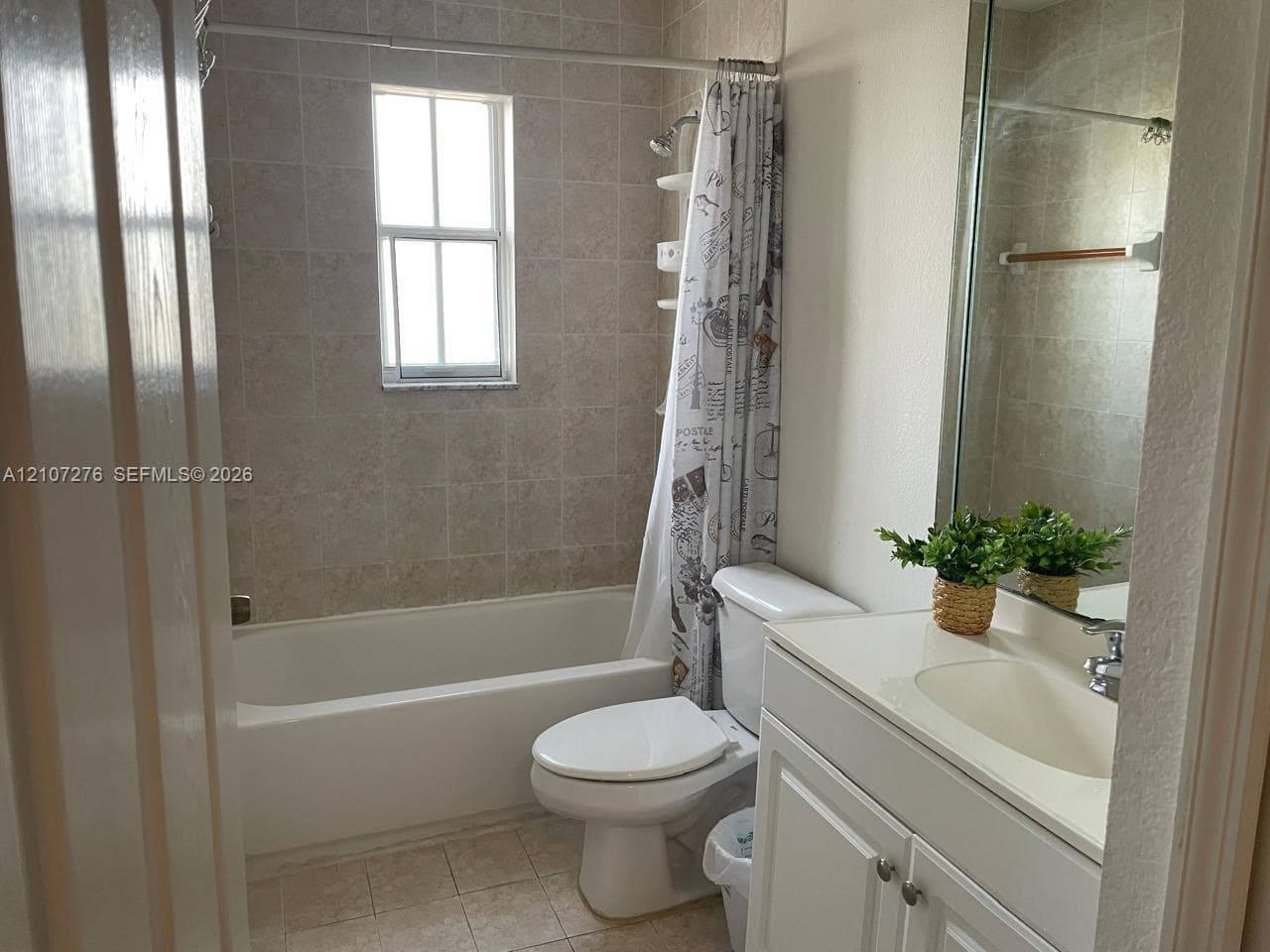 Bathroom featuring a white vanity cabinet with an integrated sink, a large wall-mounted mirror, a tub-shower combination with tiled surround, and ceramic tile flooring