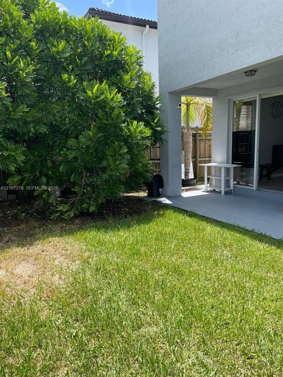 Private backyard featuring a concrete patio, exterior lighting, sliding glass door, and mature landscaping