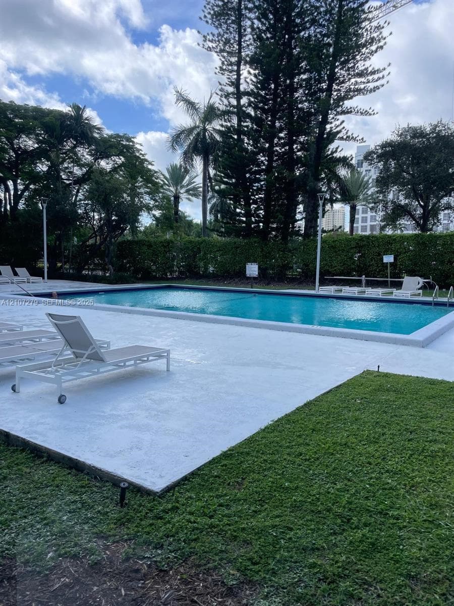 Rectangular swimming pool surrounded by a concrete deck, manicured lawn, perimeter landscaping, and mature trees