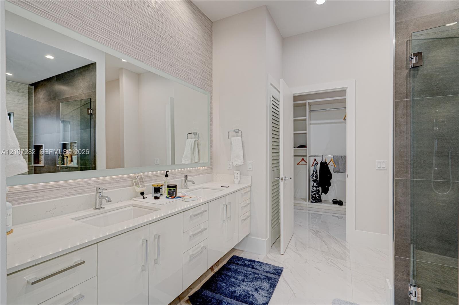 Double vanity featuring white cabinetry, quartz countertops, integrated under-mount sinks, and an expansive wall-to-wall mirror with under-cabinet lighting
