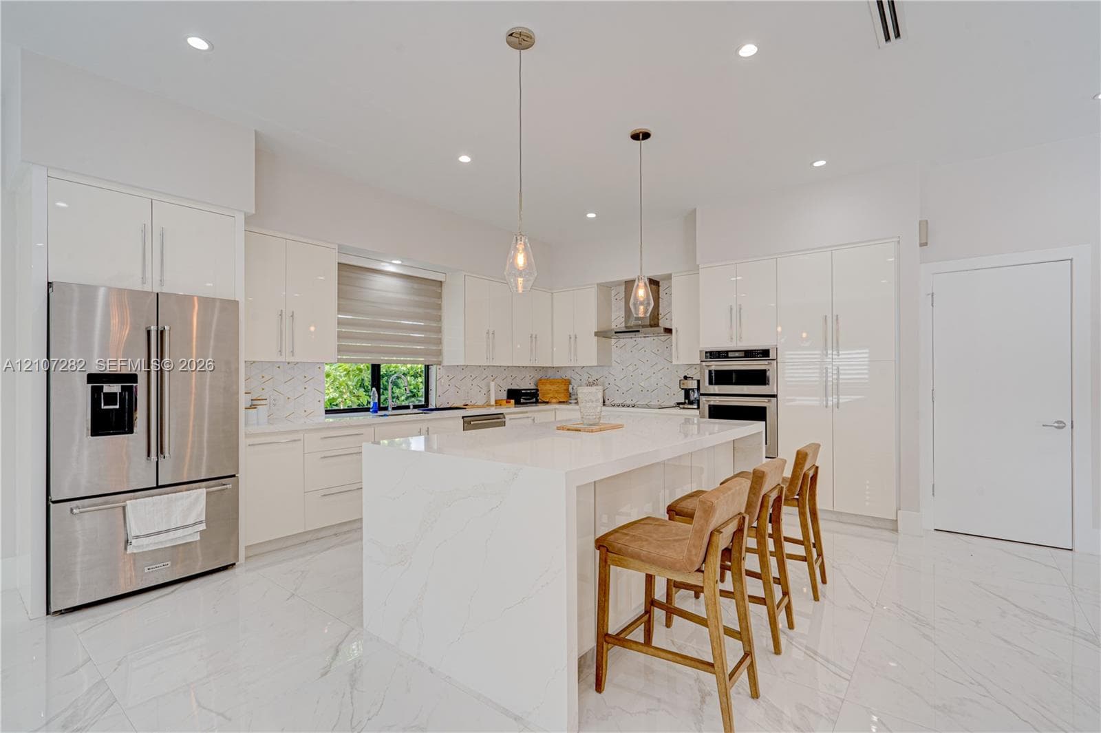 Kitchen featuring high-gloss cabinetry, stone-surfaced waterfall island, stainless steel appliances, patterned backsplash, and polished tile flooring