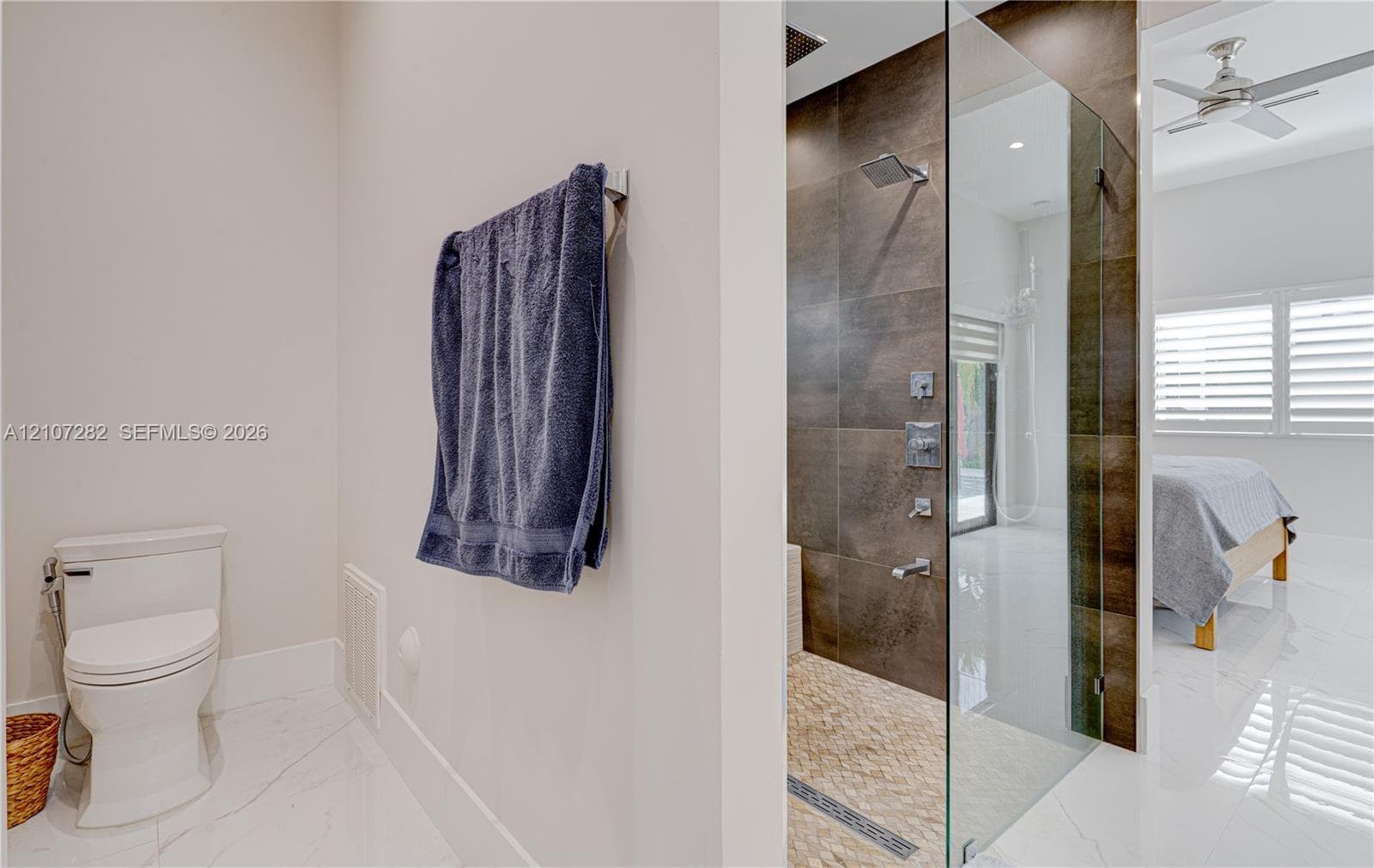 Walk-in shower with dark large-format tile surround, rainfall showerhead, and glass enclosure, complemented by porcelain flooring and a wall-mounted toilet