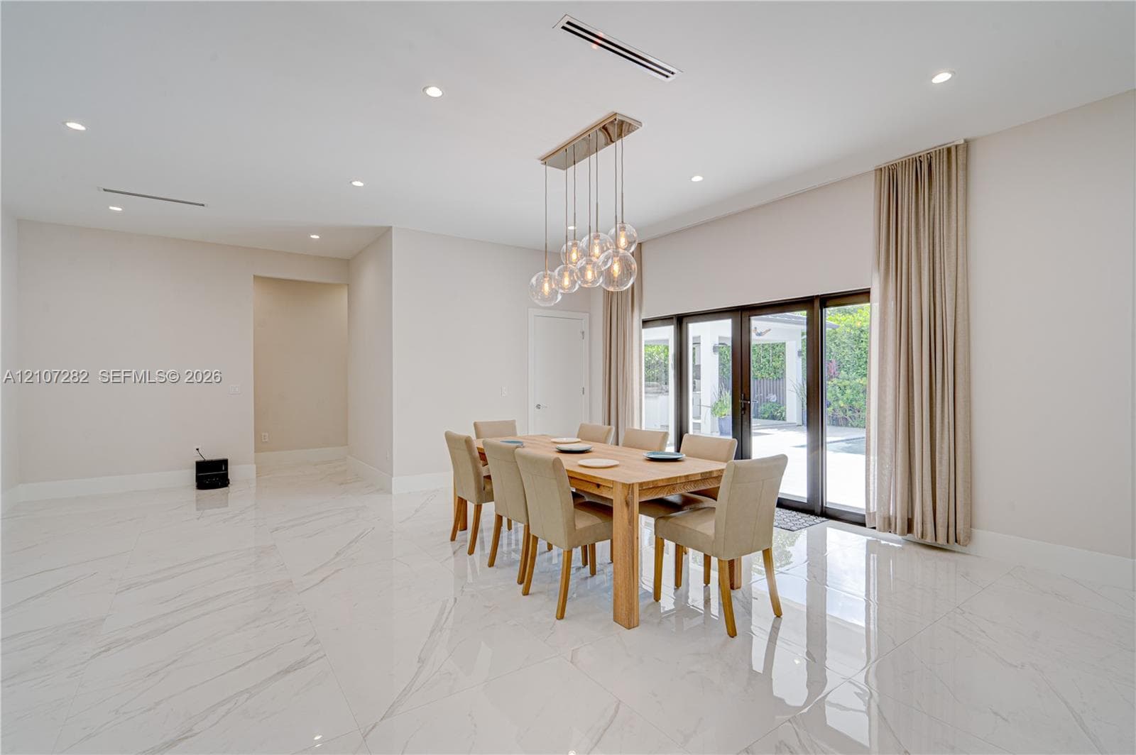 Open-concept space featuring polished stone-finish flooring, high ceilings with recessed lighting, multi-pendant spherical chandelier, and full-height glass patio doors