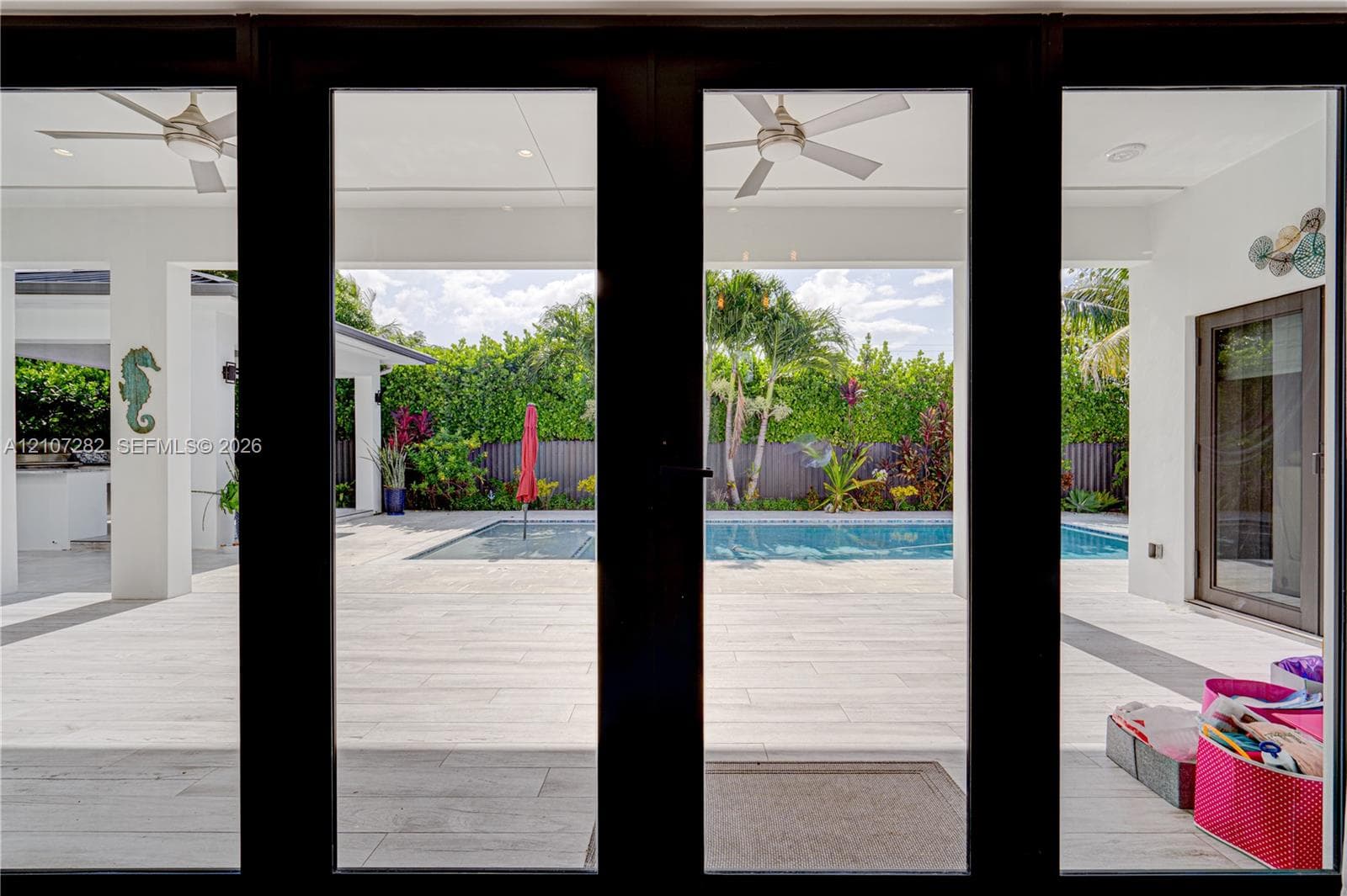 Covered patio featuring large-format tile flooring and ceiling fans, opening to an outdoor swimming pool area with privacy fencing