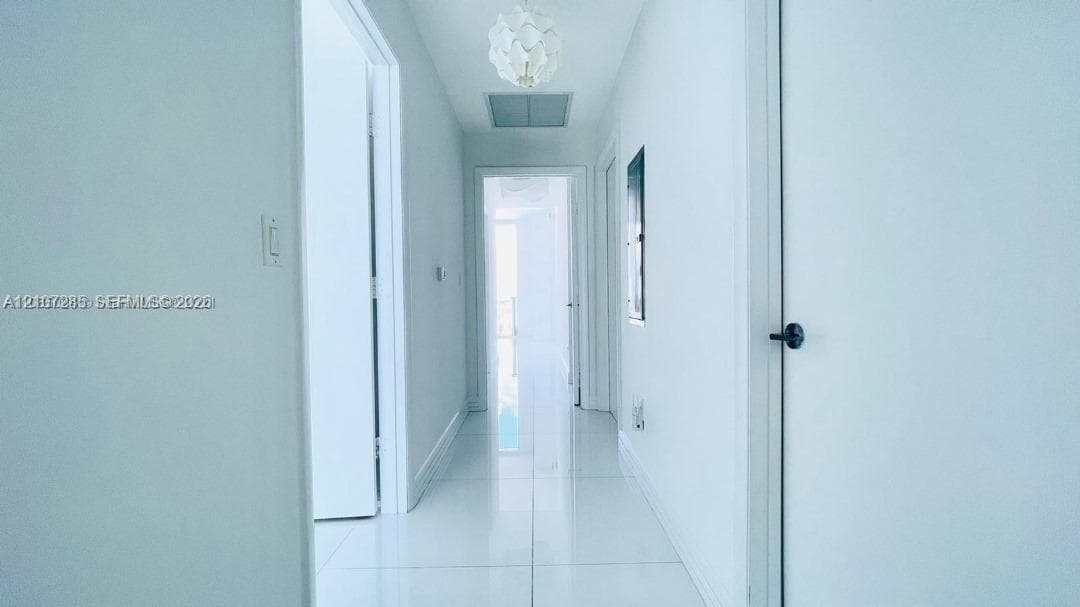 Hallway featuring high-gloss tile flooring, white interior doors with matte black hardware, and a contemporary spherical pendant light fixture