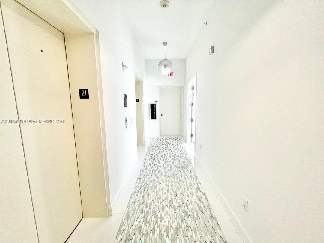 Hallway featuring neutral-toned walls, polished tile flooring, patterned runner carpet, and a spherical pendant light fixture