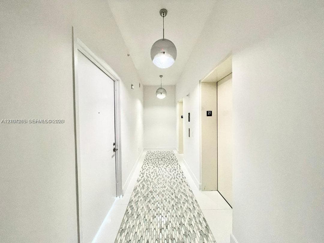 Hallway featuring crisp white walls, large-format tile flooring with a patterned mosaic inlay, and dual spherical pendant lighting fixtures