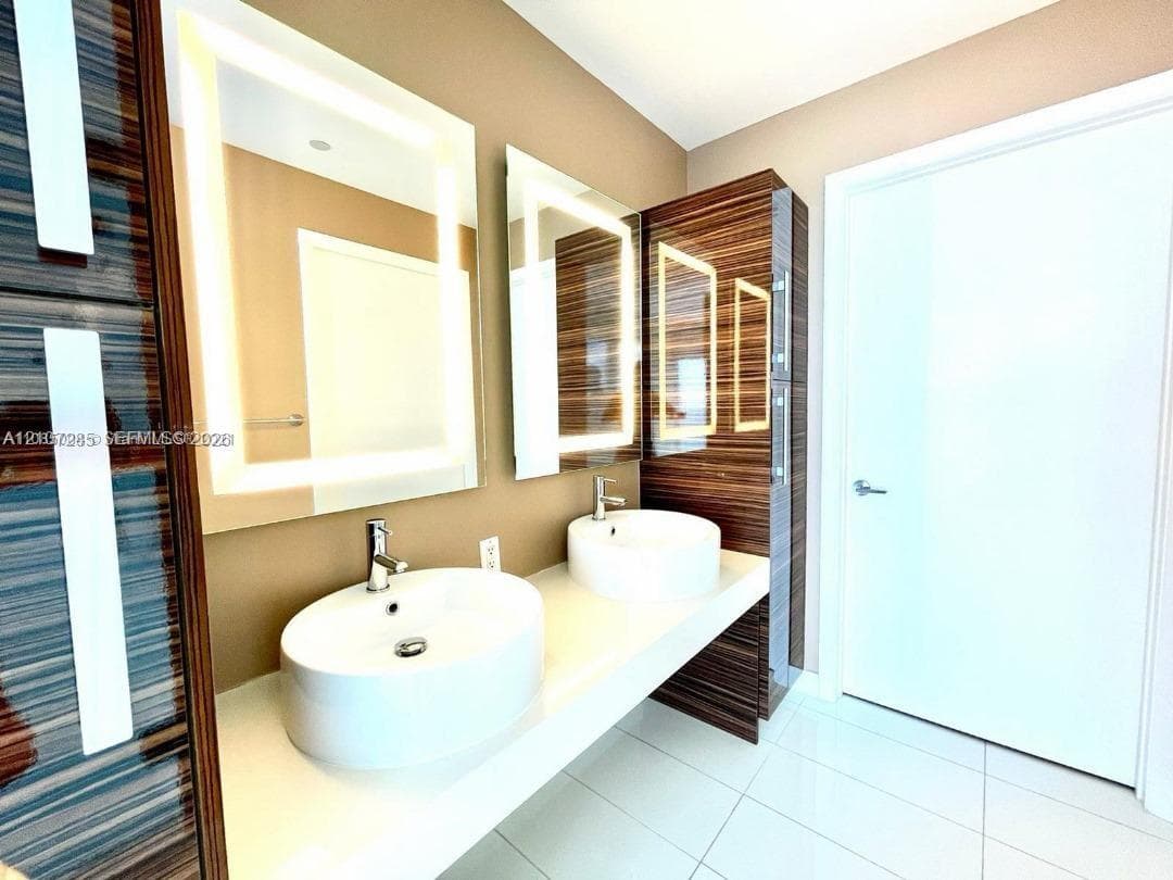 Floating double vanity featuring rectangular vessel sinks, quartz countertop, integrated wood-finish cabinetry, and back-lit mirrors with chrome faucets