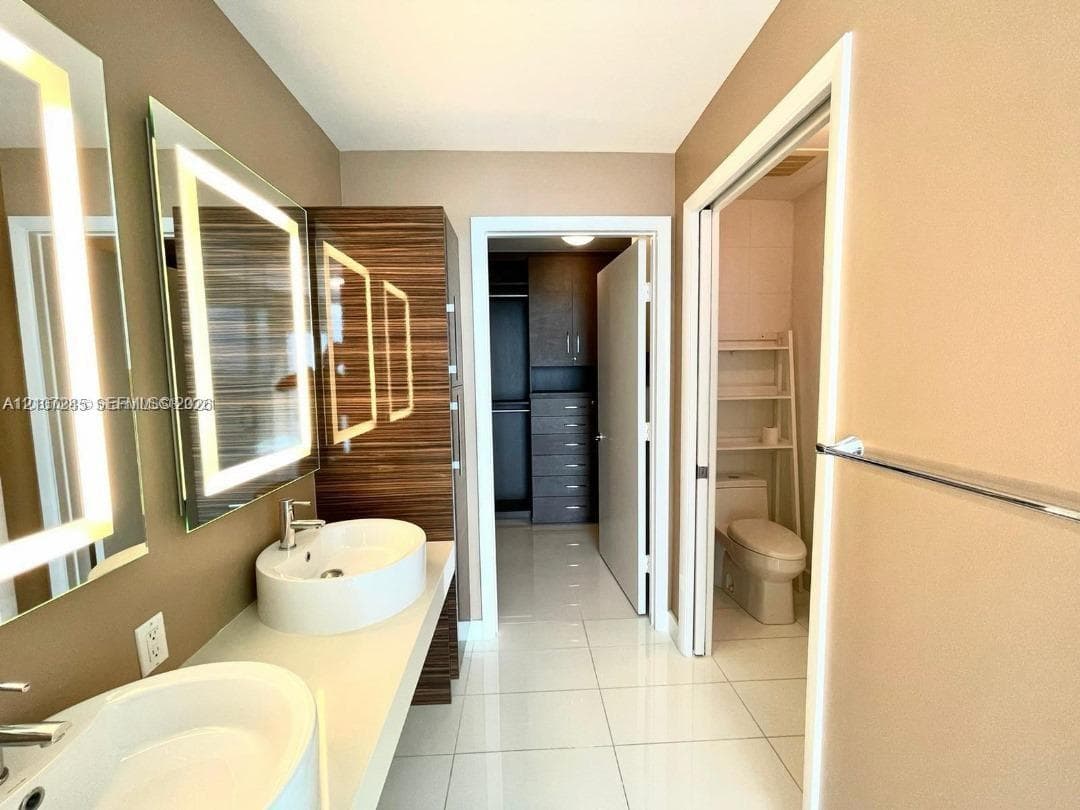 Dual floating vanity with rectangular vessel sinks, LED-backlit mirrors, wood-finish cabinetry, and porcelain tile flooring