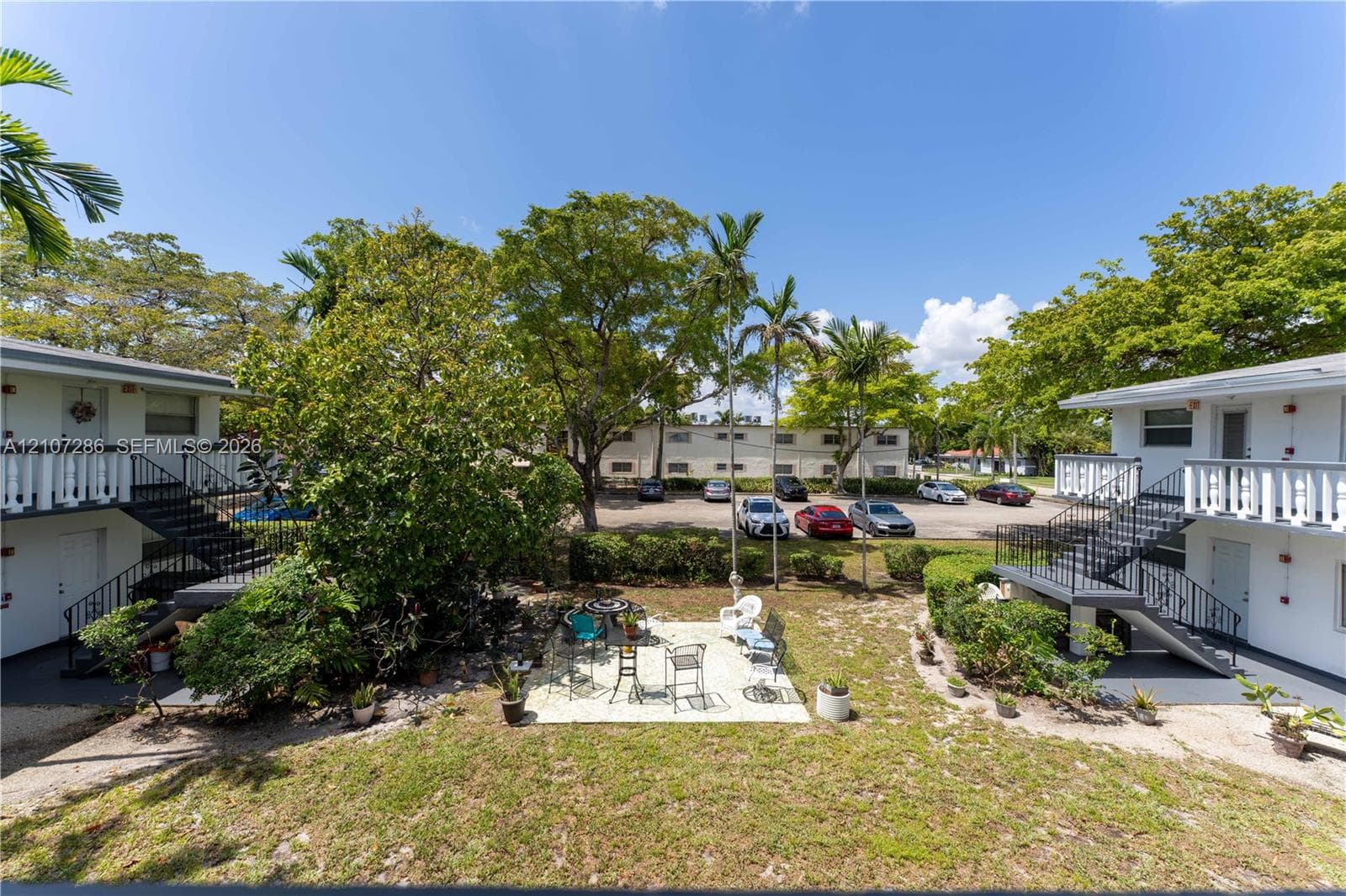 Exterior grounds featuring a paved patio, mature trees, manicured landscaping, metal exterior staircases, and white balustrade railings