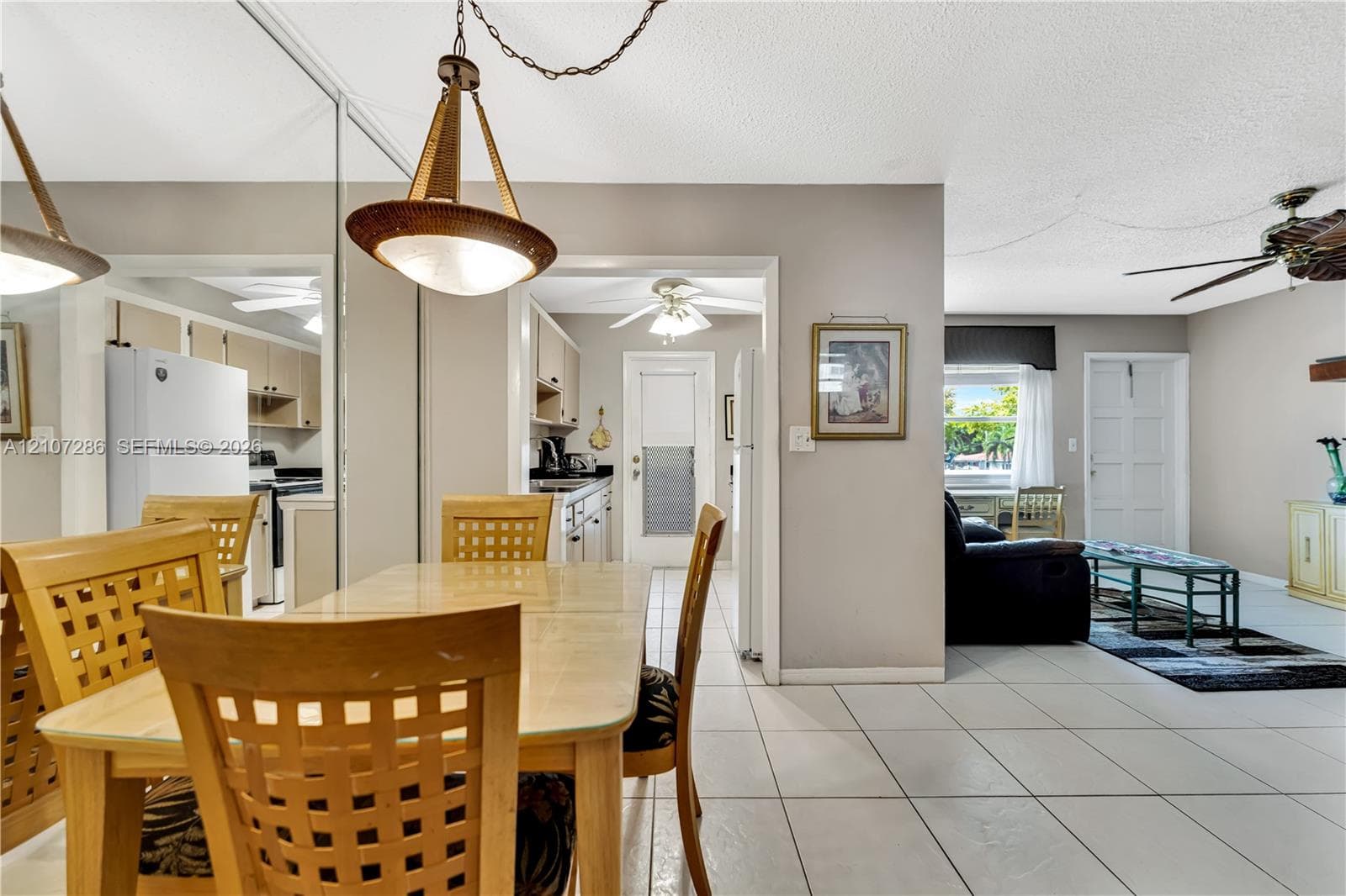 Open-concept interior featuring oversized wall mirrors, neutral tile flooring, a multi-light pendant fixture, ceiling fans, and a classic paneled exterior door