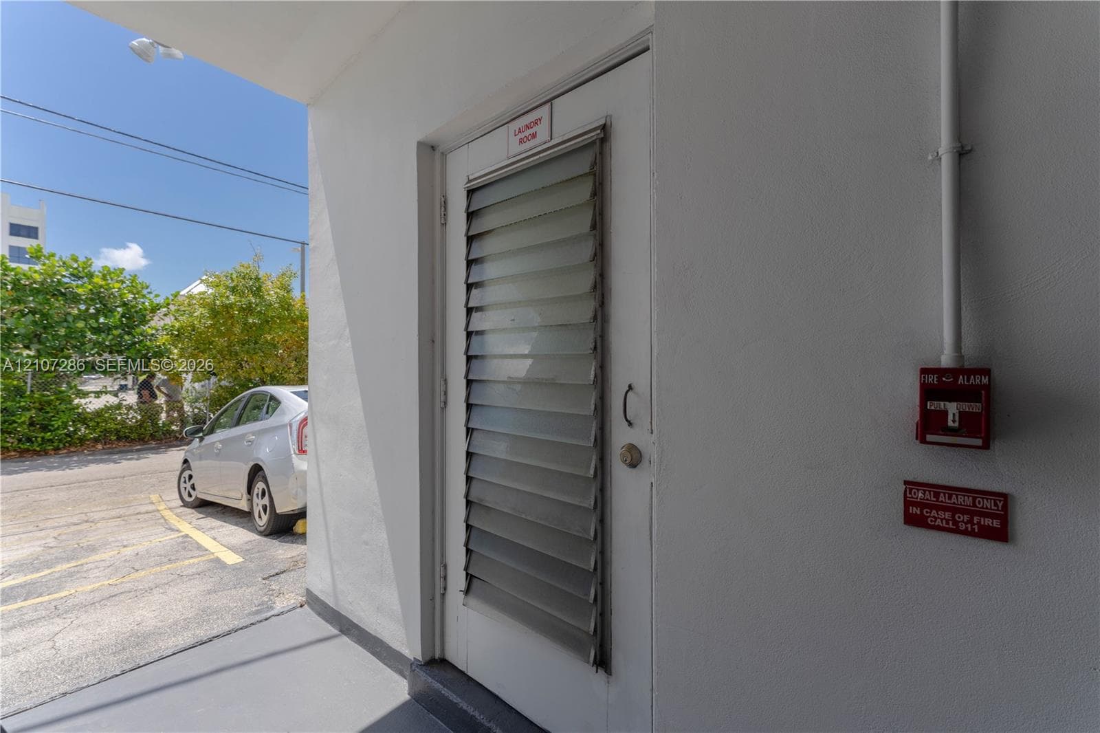Exterior door featuring integrated jalousie window panels, smooth stucco wall finish, and a mounted fire alarm system