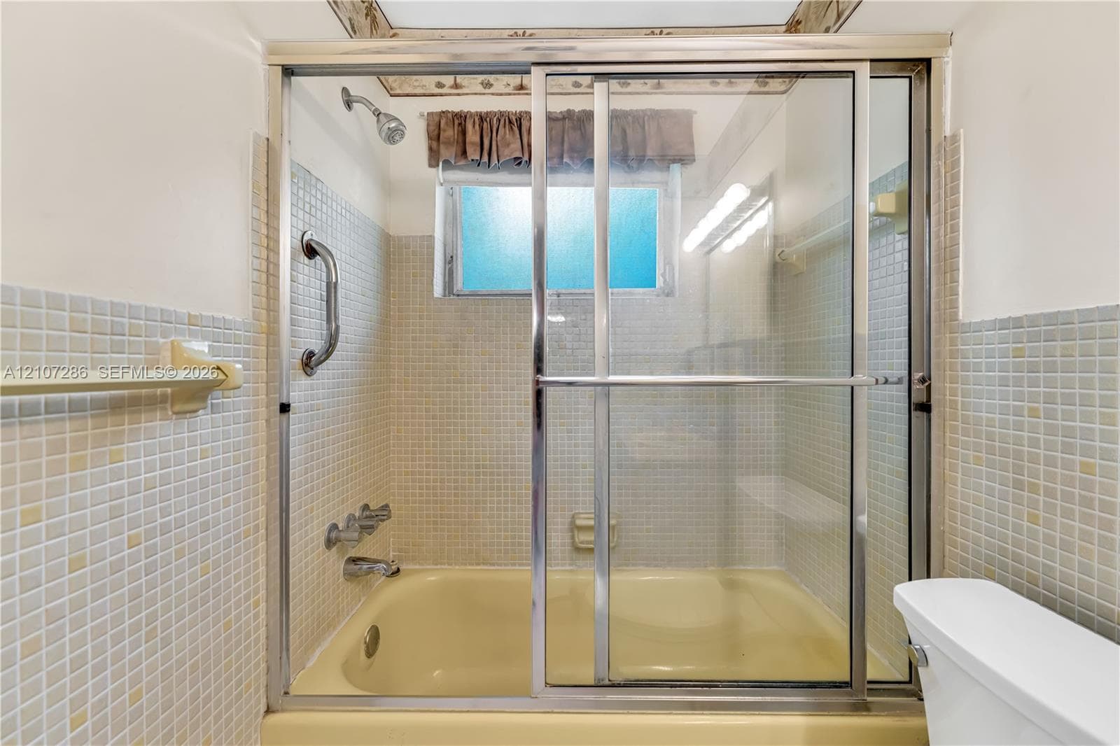 Bathtub featuring a glass sliding enclosure, mounted chrome faucet fixtures, and square mosaic wall tile surrounds