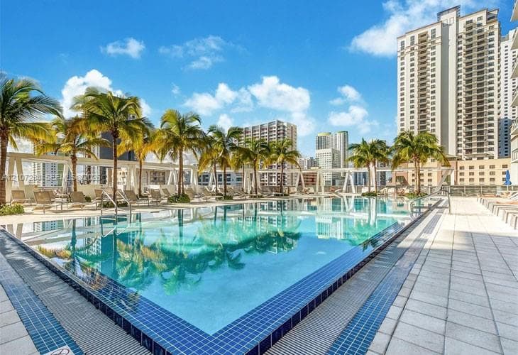 Rooftop swimming pool featuring a tiled deck, surrounding palm trees, and perimeter structural framework