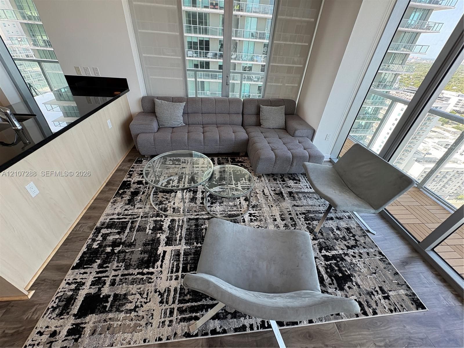 Floor-to-ceiling windows, wood-finish flooring, and kitchen island with black countertop