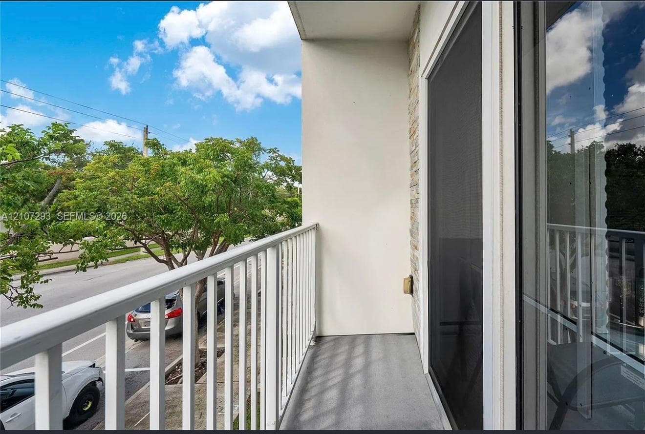 Balcony featuring white metal railings, stone-finish exterior accents, and sliding glass entry doors