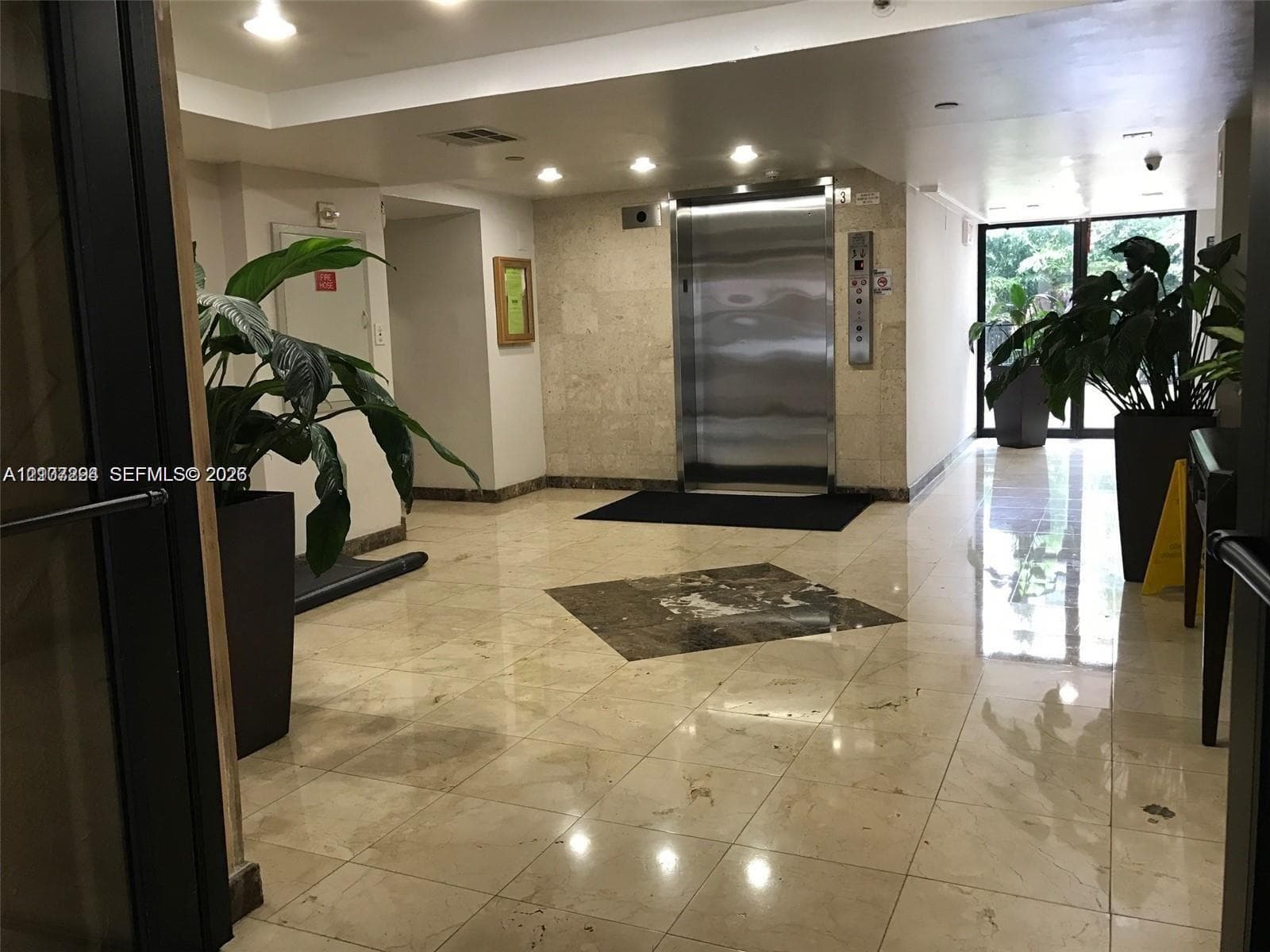 Elevator lobby featuring polished stone flooring with an inlaid stone medallion, recessed lighting, and a stainless steel elevator door