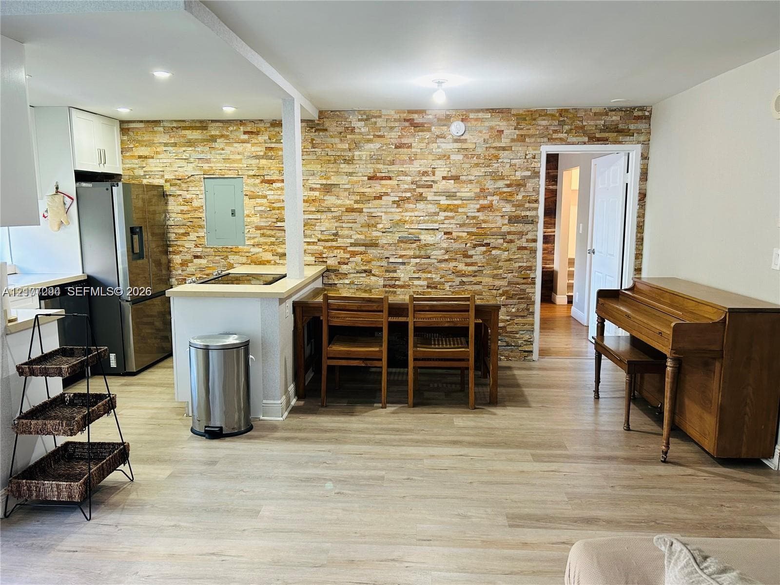 Interior space featuring a floor-to-ceiling stone veneer accent wall, wood-finish flooring, and a kitchen peninsula with a stainless steel refrigerator