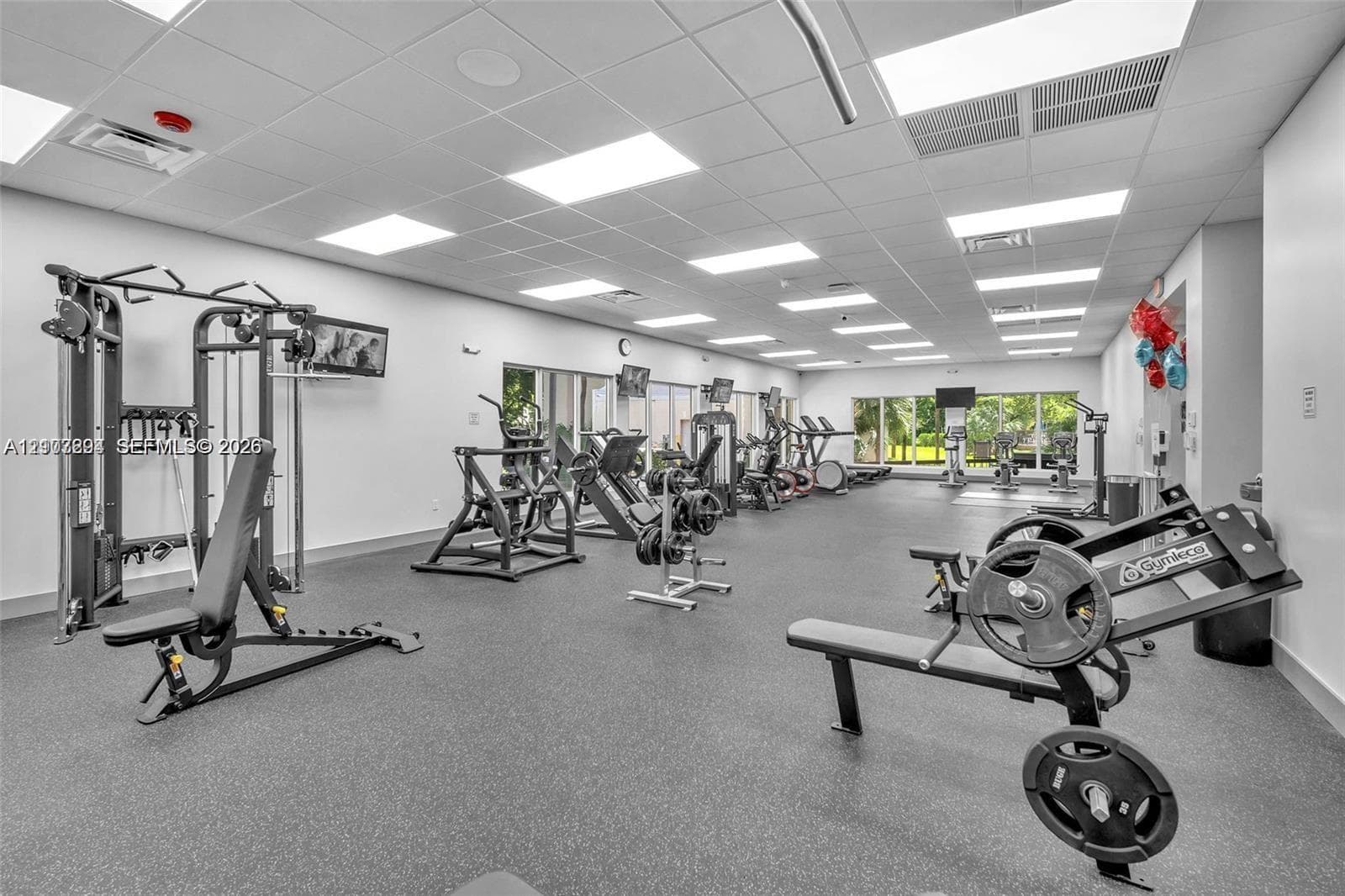 Fitness center featuring recessed drop-ceiling lighting, resilient rubberized flooring, and expansive windows
