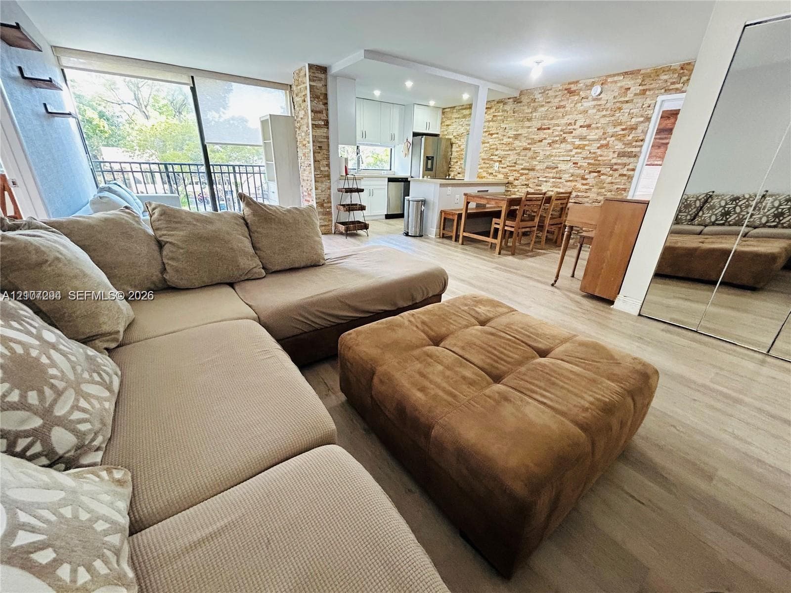 Open-concept living space featuring wood-finish flooring, a full-height stone veneer accent wall, recessed lighting, and glass sliding doors providing exterior access