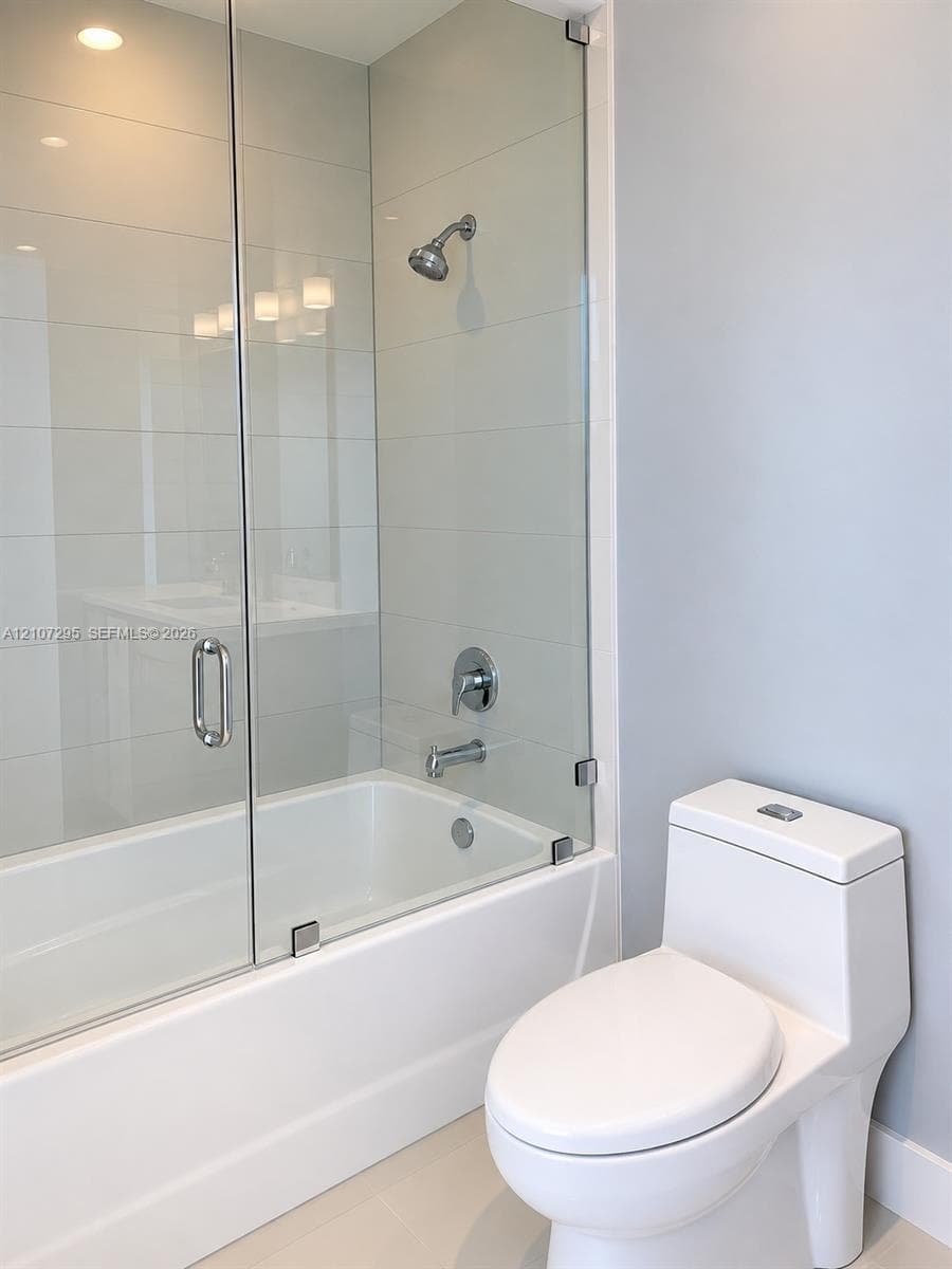 Bathroom featuring a tub-shower combination with floor-to-ceiling tile surround, a frameless glass door, chrome fixtures, and a dual-flush toilet