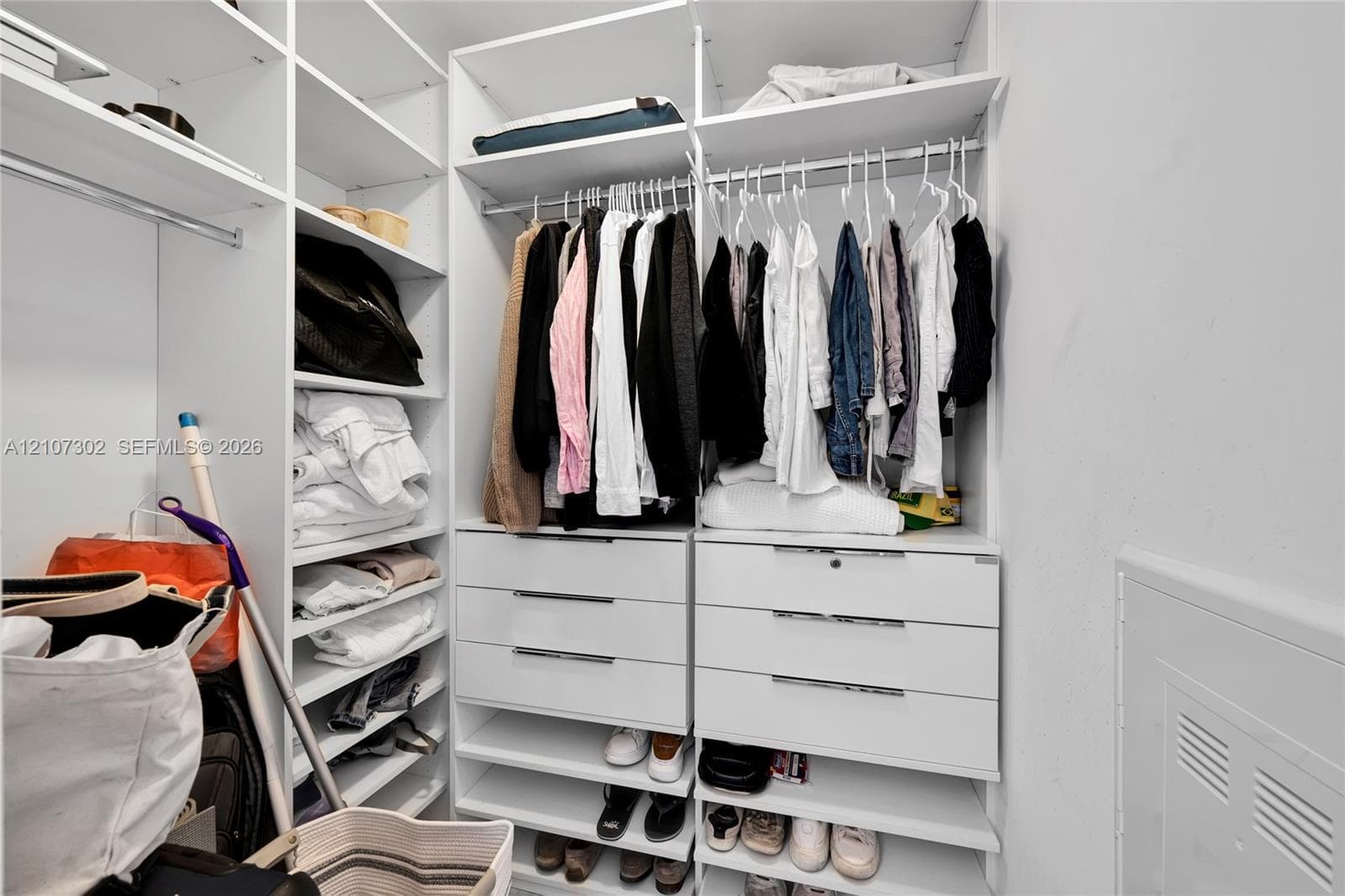 Walk-in closet featuring white built-in shelving, multiple hanging rods, and six integrated soft-close drawers with metallic pulls