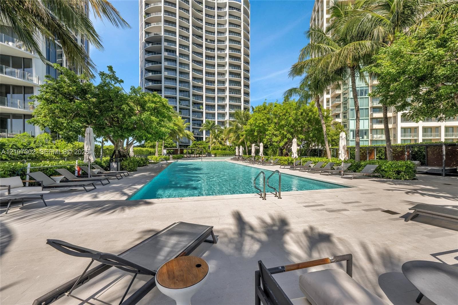 Swimming pool featuring stone pavers, metal pool ladder, and palm tree landscaping