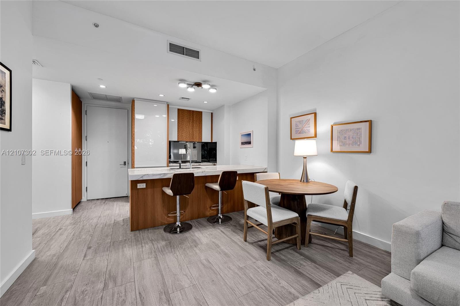 Kitchen featuring a stone-topped island with wood-finish cabinetry, floor-to-ceiling high-gloss white pantry storage, and wood-finish flooring