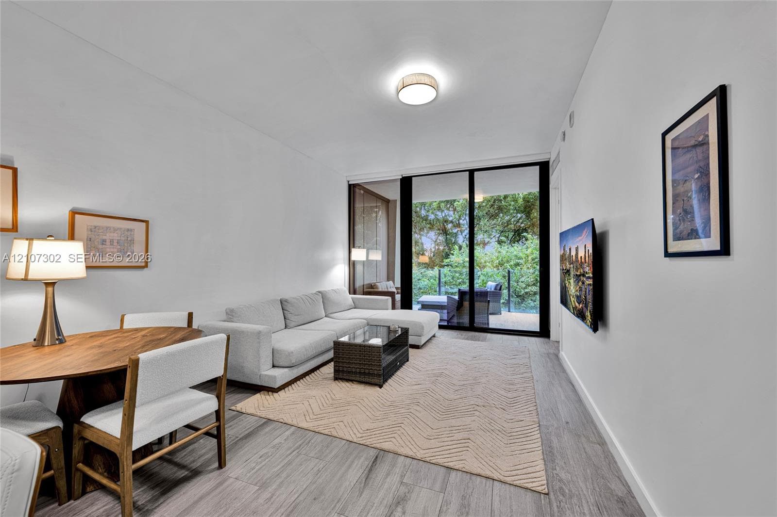 Open-concept interior featuring wood-finish flooring, a flush-mount circular ceiling fixture, and floor-to-ceiling sliding glass doors leading to an exterior balcony