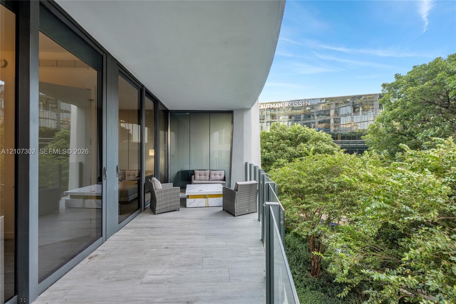 Covered balcony featuring large-format stone-finish tile flooring, floor-to-ceiling glass paneling, and a clear glass railing
