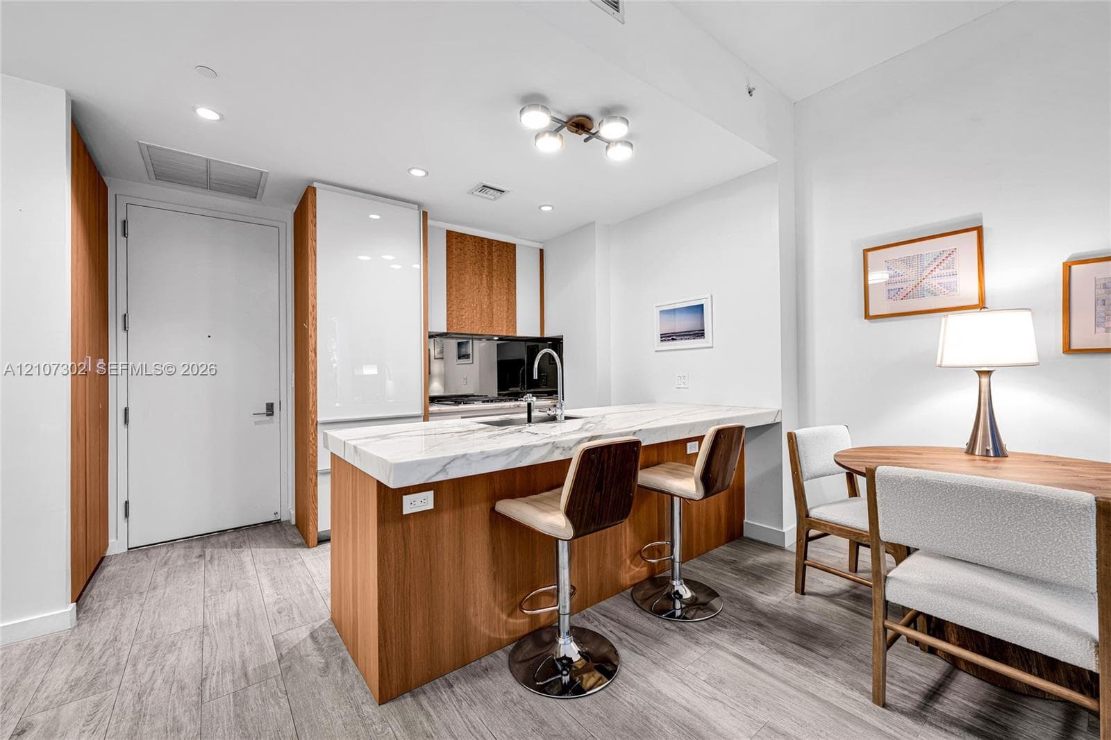 Kitchen featuring wood-finish cabinetry, white high-gloss paneling, integrated refrigerator, stone-composite countertop with waterfall edge, and wood-finish flooring