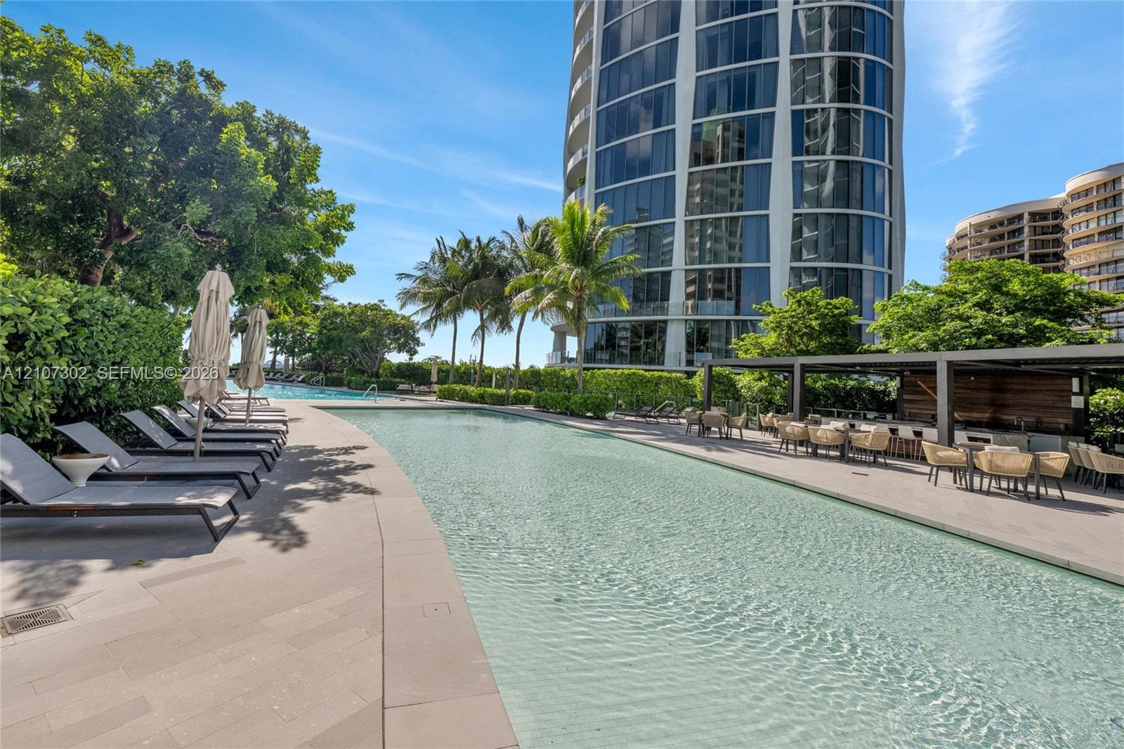 Swimming pool featuring stone-tile decking, a covered outdoor bar area, and mature landscaping
