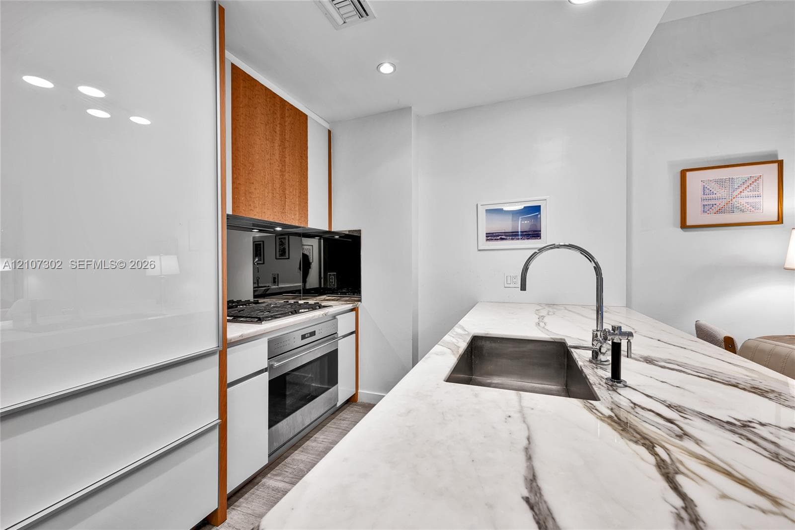 Contemporary kitchen featuring white high-gloss cabinetry, stone-surface countertops, an undermount sink with a gooseneck faucet, stainless steel wall oven, and a gas cooktop with a mirrored backsplash