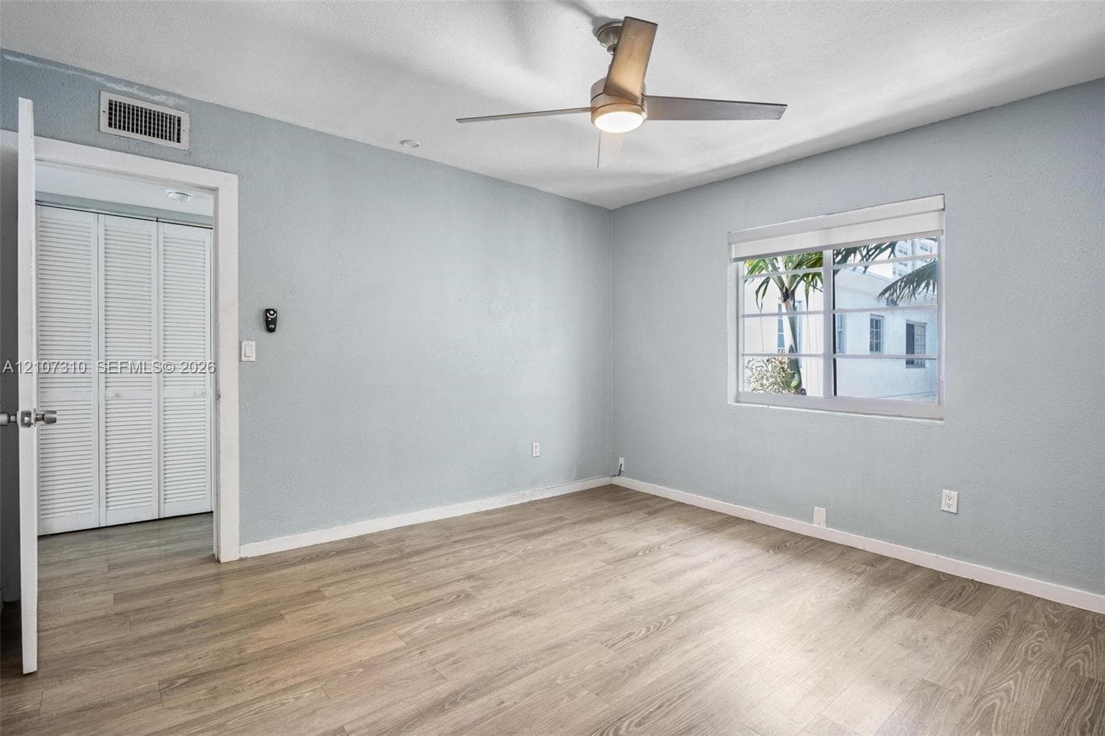 Interior space featuring wood-finish flooring, a contemporary ceiling fan with integrated lighting, dual bifold closet doors, and a multi-pane window