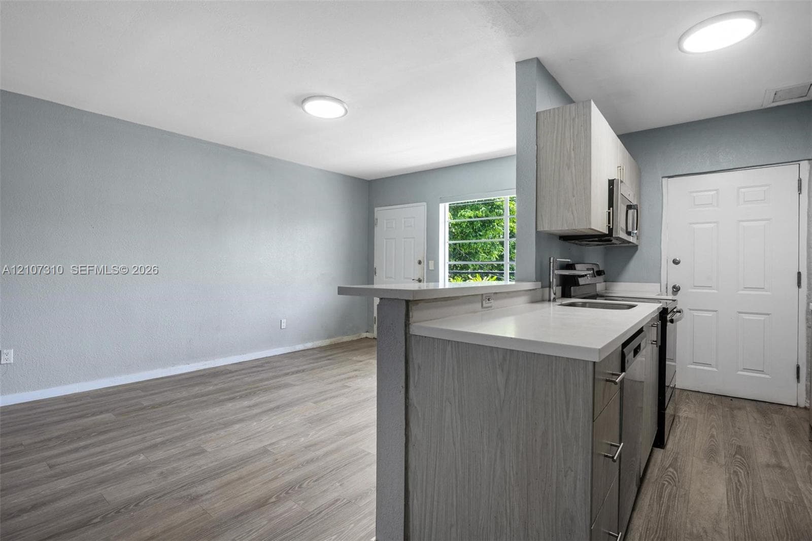 Kitchen featuring wood-finish cabinetry, white countertops, a stainless steel sink, and wood-finish flooring throughout