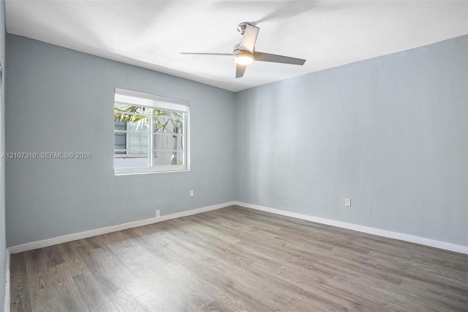 Neutral-toned room featuring wood-finish flooring, a horizontal sliding window, and a ceiling-mounted light fixture with a fan