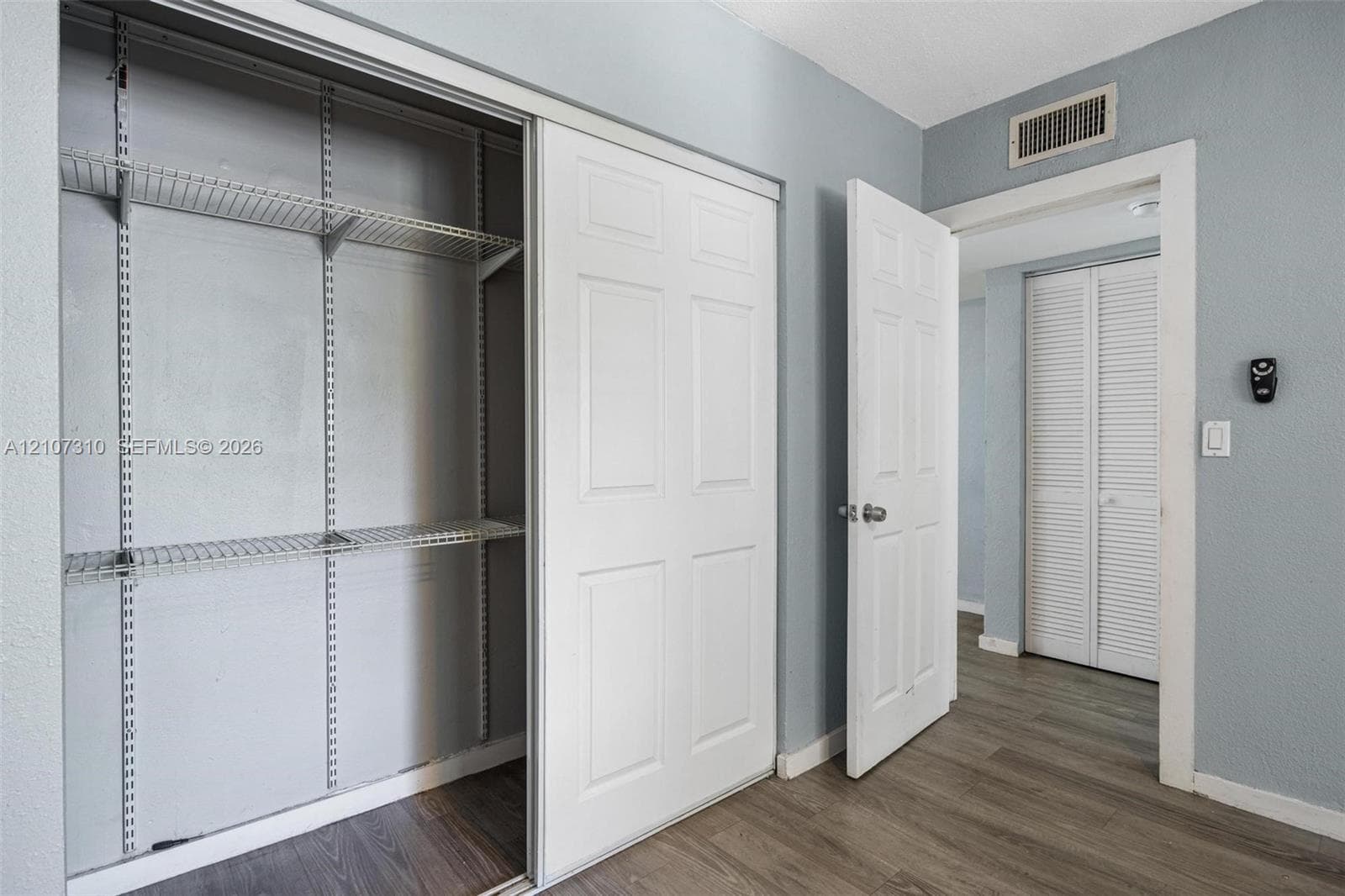 Interior space featuring wood-finish flooring, white four-panel sliding closet doors, built-in wire shelving, and white louvered closet doors