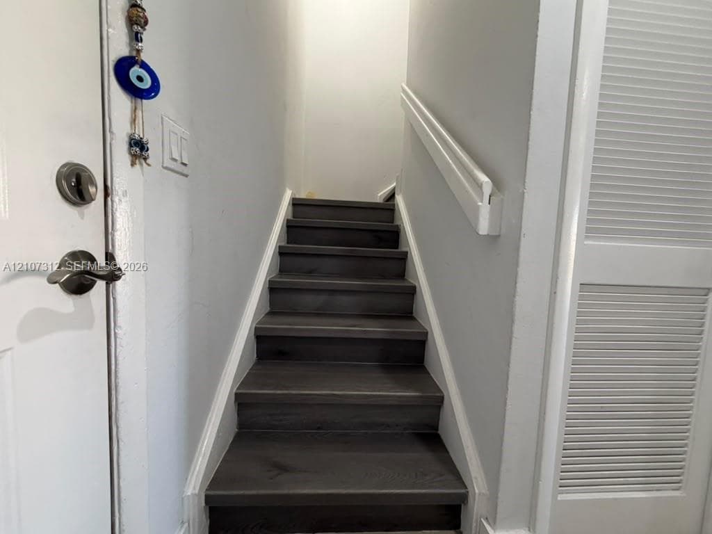 Staircase featuring wood-finish treads and a white wall-mounted handrail, complemented by a louvered-panel closet door
