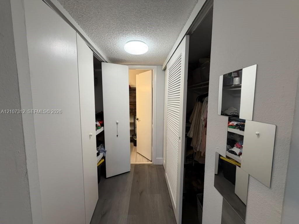 Hallway featuring wood-finish flooring, flush-mount ceiling lighting, bi-fold closet doors, and louvered storage doors