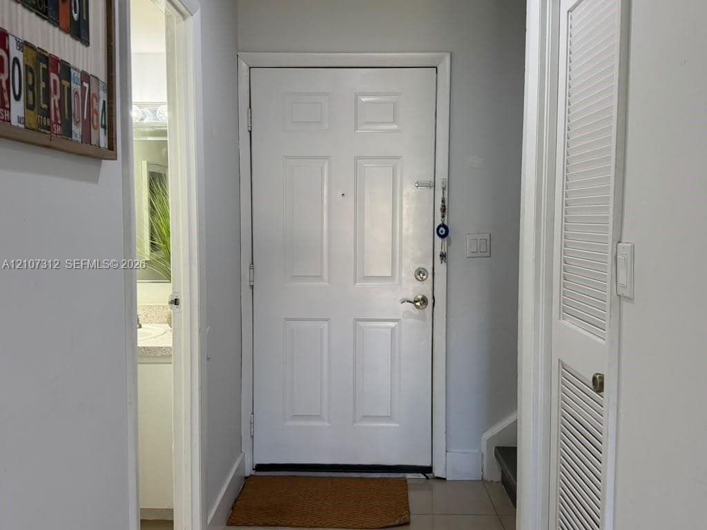 Six-panel solid door with brushed metal hardware, tile flooring, and louvered closet door