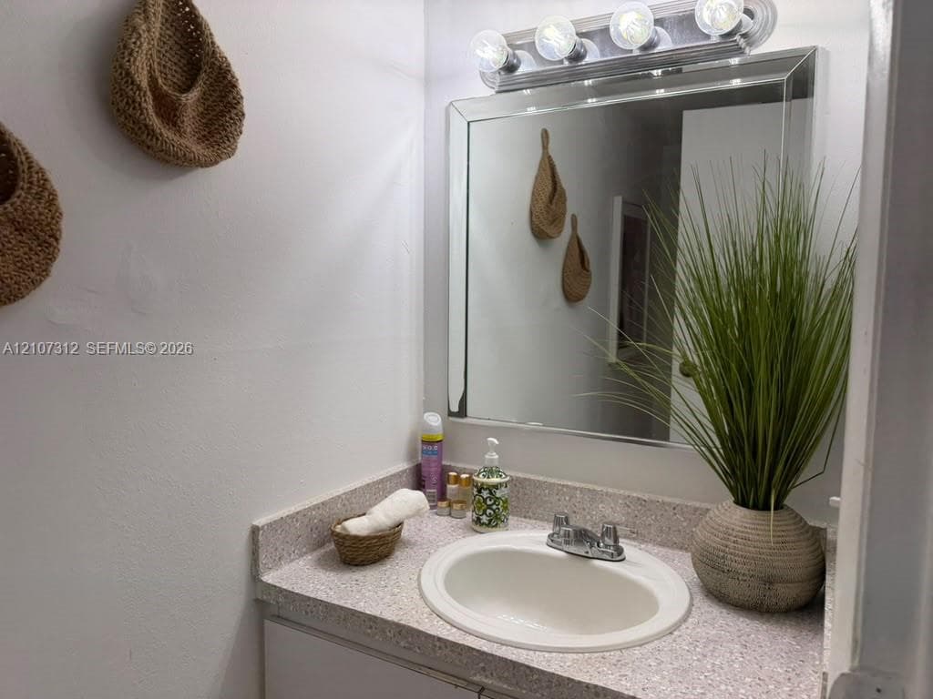 Vanity featuring a stone-composite countertop, integrated oval basin, polished chrome faucet, and a large beveled-edge mirror with a multi-bulb light fixture