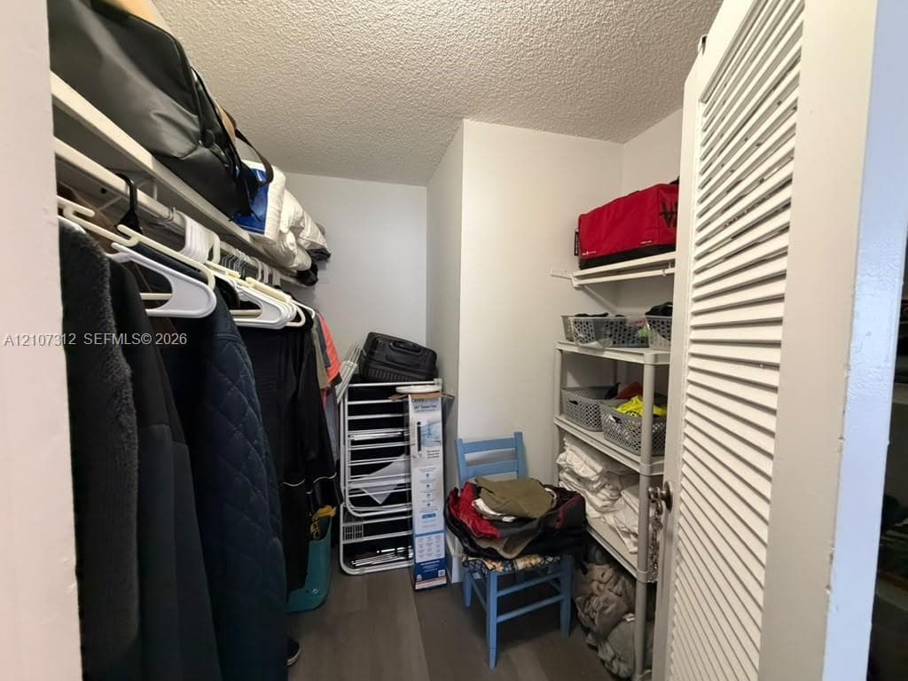 Walk-in storage space featuring wood-finish flooring, white wire shelving, and a louvered entry door