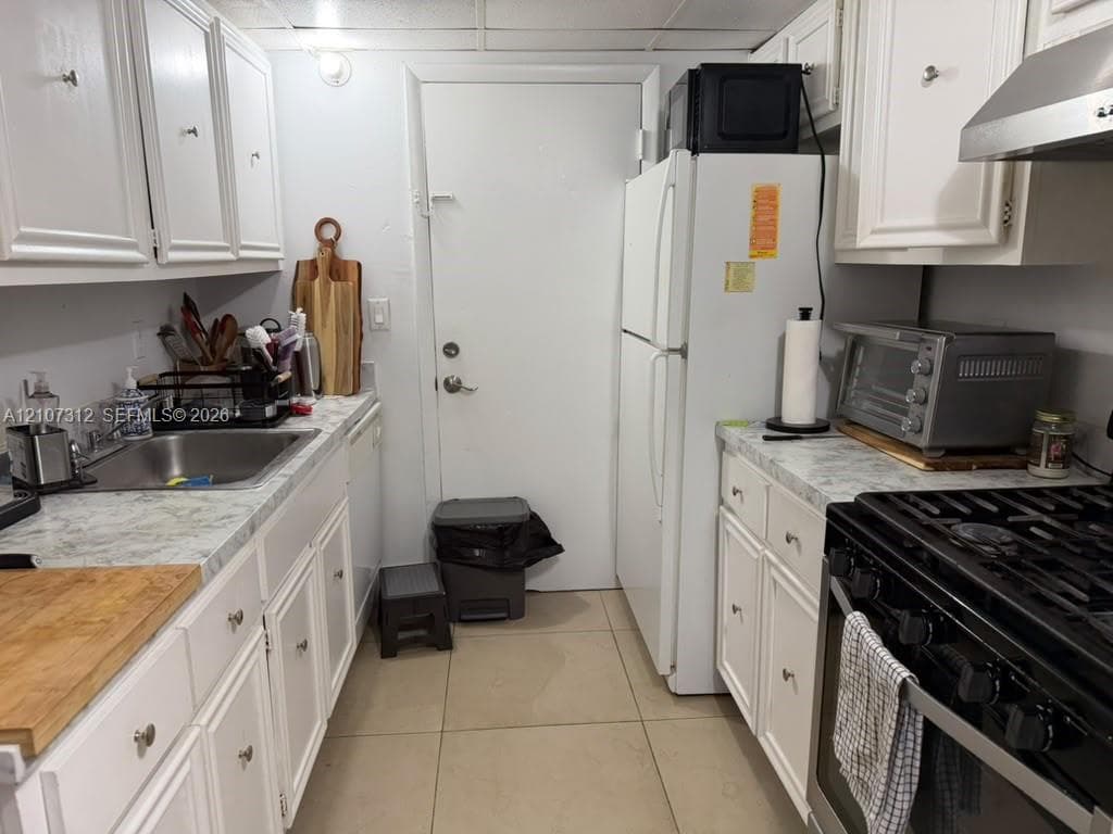 Kitchen featuring white cabinetry, stone-patterned laminate countertops, stainless steel sink, gas range, and a stainless steel range hood