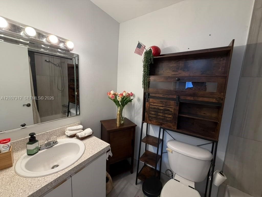 Bathroom featuring a vanity with an integrated basin, a speckled composite countertop, a framed wall mirror, and a multi-bulb vanity light fixture