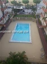 Rectangular in-ground swimming pool featuring a perimeter fence, paved deck, and surrounding palm trees