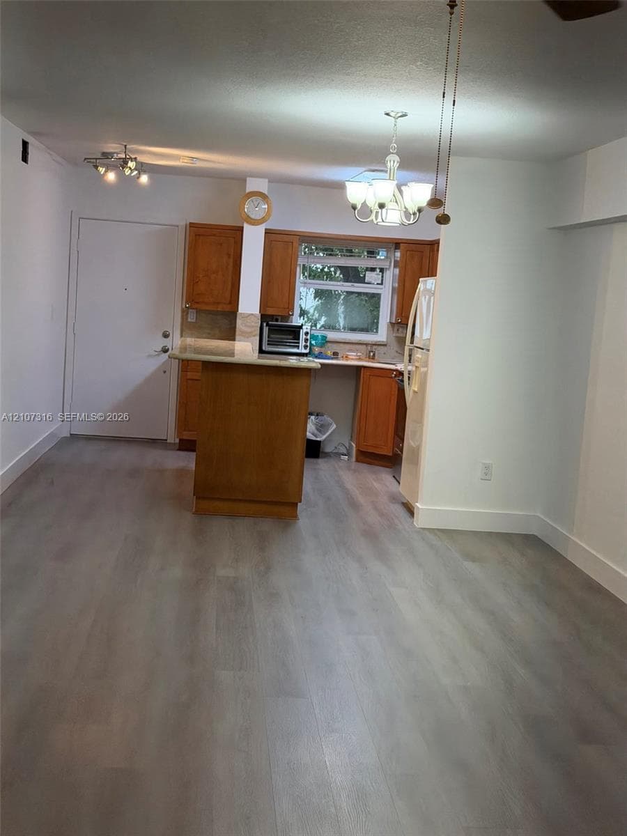 Kitchen featuring wood cabinetry, a center island with a solid surface countertop, wood-finish flooring, and decorative hanging light fixtures